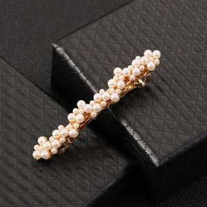 Détail d'une pince à cheveux élégante avec perles et métal doré sur boîte noire texturée
