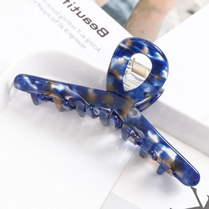 Detail of blue acetate hair claw clip with gold spring on a white tray with a magazine