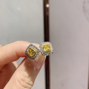 Close-up of silver earrings with a square yellow gemstone and sparkling zircon border