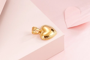 Detailed view of a gold heart pendant with textured beaded edges on a pink background