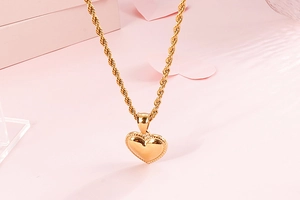 Detail of a gold heart pendant necklace with beaded edges on a twisted rope chain