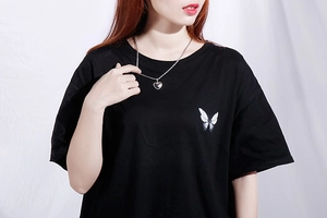 Close-up of a silver heart pendant necklace styled on a black butterfly print t-shirt