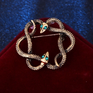 Macro shot of twin snake brooch with green gemstone eyes on red velvet background