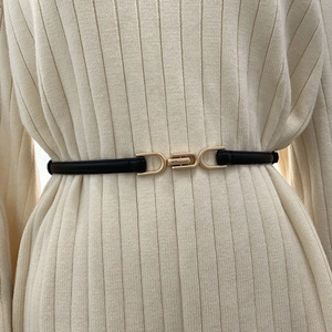 Slim black leather belt with unique gold metal buckle worn over white knit sweater