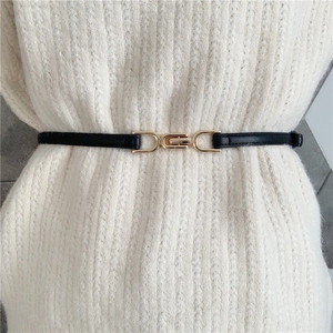 Detail of thin black PU leather belt with gold metal clasp on white knit sweater