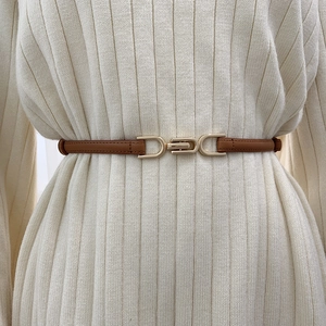 Close-up of a slim brown leather belt with a gold buckle on a white knitted dress