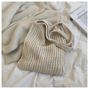 Primer plano de bolso tote de punto beige con textura gruesa y asas largas sobre lino