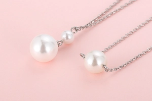 Detail of silver chain necklace with lustrous white pearls on a soft pink background