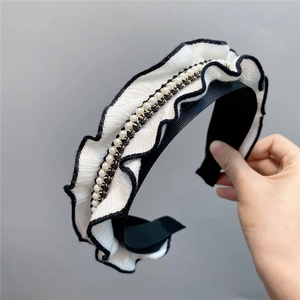 Close-up of knitted ruffle headband with pearls and gold chain details in black and white