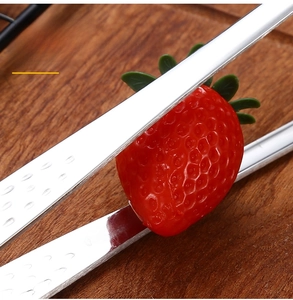 Macro detail of 304 stainless steel kitchen tongs picking up a fresh strawberry