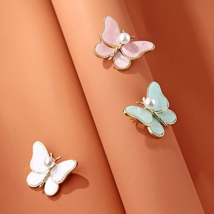 Detailed macro view of pearl butterfly brooches in pink, mint green and white finishes