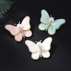 Detailed view of alloy butterfly brooches with pearlescent wings in pink, green, and white