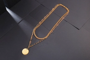 Close-up of double-layered gold chain necklace with round pendant and paperclip link