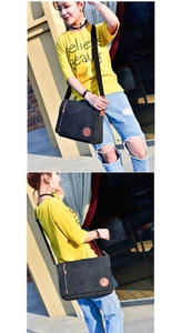 Detail of black canvas messenger bag featuring leather accents and adjustable strap