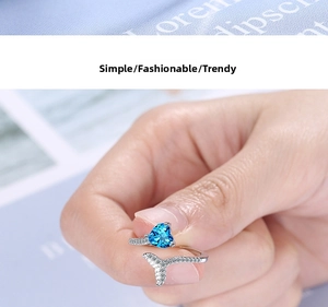 Detailed close-up of heart-shaped blue stone and crystal fishtail on an open ring