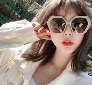 Close-up of oversized cream hexagonal sunglasses with gradient brown lenses on model