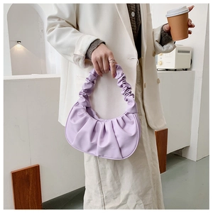 Close-up of lilac purple pleated dumpling bag held by a model in a minimal setting