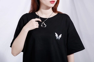 Pendentif cœur en argent avec cristaux porté sur un t-shirt noir imprimé papillon