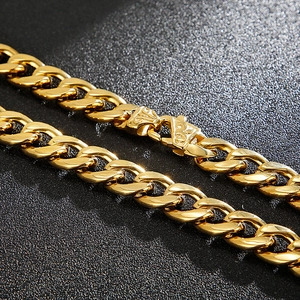 Flat Cuban chain necklace in gold finish with intricate clasp on black background