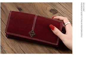 Detail of dark red vintage wallet with white stitching and floral metal button on wood