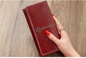 Detail of red vintage leather wallet featuring white stitching and floral metal charm