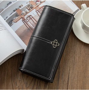 Detail of black leather long wallet with white stitching and golden clover metal buckle