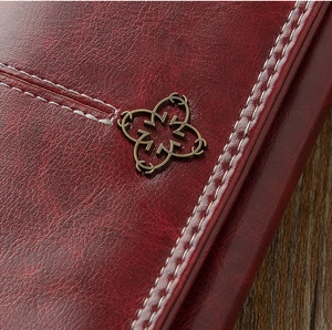 Macro shot of burgundy vintage leather wallet featuring delicate white stitching and a bronze badge