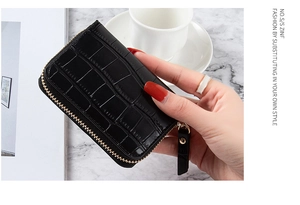 Macro view of compact black crocodile pattern card holder with gold zipper detail