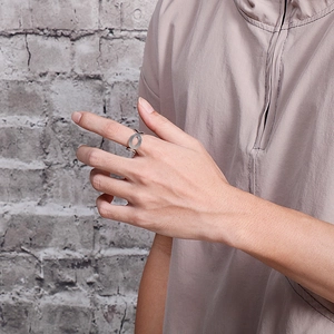 Modern hollow number 8 stainless steel open ring worn on finger against brick wall