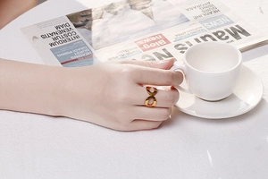 Nahaufnahme eines goldenen Infinity-Rings an einer Frauenhand mit Kaffeetasse