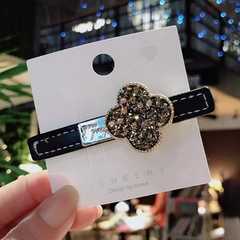 Macro detail of black leather hair clip with gold clover and sparkling dark crystals