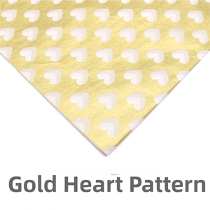 Macro shot of gold tissue paper featuring a repeated white heart pattern and metallic texture