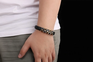 Close-up of men's black woven leather bracelet with gold and silver horseshoe buckle