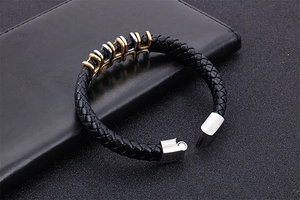 Detail of black braided leather bracelet with gold and silver metal rings and magnetic clasp