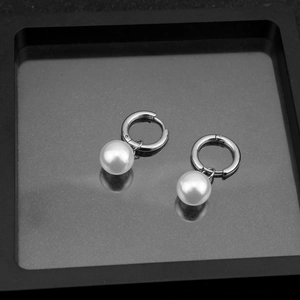 Detailed view of white pearl drop earrings on a matte black tray with silver hoop metal