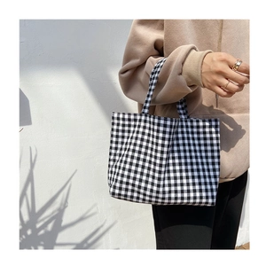 Detail view of a black and white checkered cotton linen handbag with soft sunlight shadows