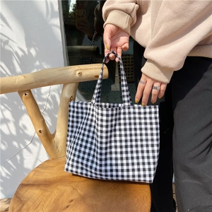 Lifestyle shot of black and white plaid canvas tote bag on a wooden chair outdoors