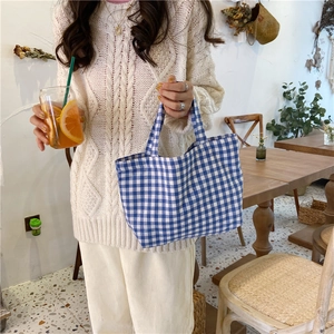 Detail of blue and white plaid cotton linen tote bag held by a model in a cafe