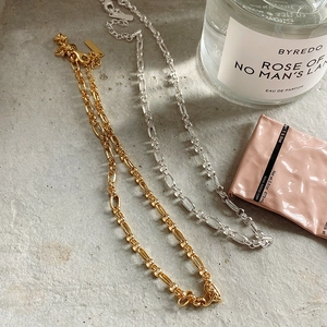 Detail of gold and silver bold chain necklaces with lobster clasp on a textured surface