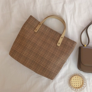 Detail view of the brown check pattern fabric and cream leather handle with metal rivets