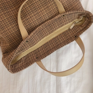 Close-up of vintage brown plaid tote bag with leather handles and metal zipper closure