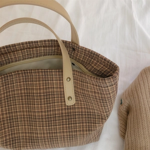 Detail view of the brown plaid tote bag with beige leather handle and metal rivets