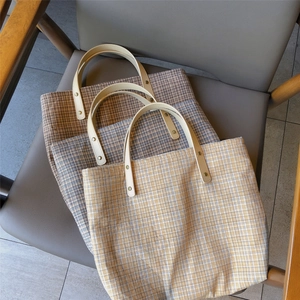 Three vintage plaid fabric tote bags with leather handles on a gray leather chair