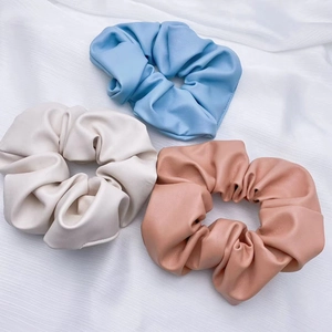 Close-up of three soft PU leather scrunchies in light blue, beige, and pink colors