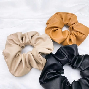 Flat lay of premium PU leather scrunchies in black, beige, and brown with soft folds