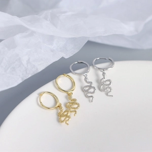 Macro detail of gold and silver S925 sterling silver snake earrings on white ceramic