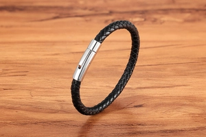 Detail of black braided leather bracelet with silver stainless steel clasp on wood