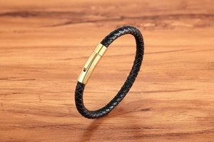 Detail of black braided leather bracelet featuring a magnetic gold metal clasp on wood