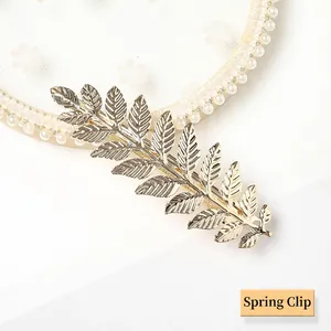 Detail of a golden alloy leaf spring clip with intricate veins on a pearl lace background