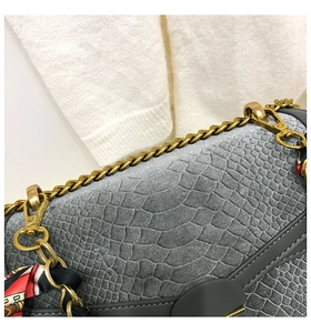 Dettaglio borsa grigia motivo coccodrillo con catena dorata e foulard di seta rossa